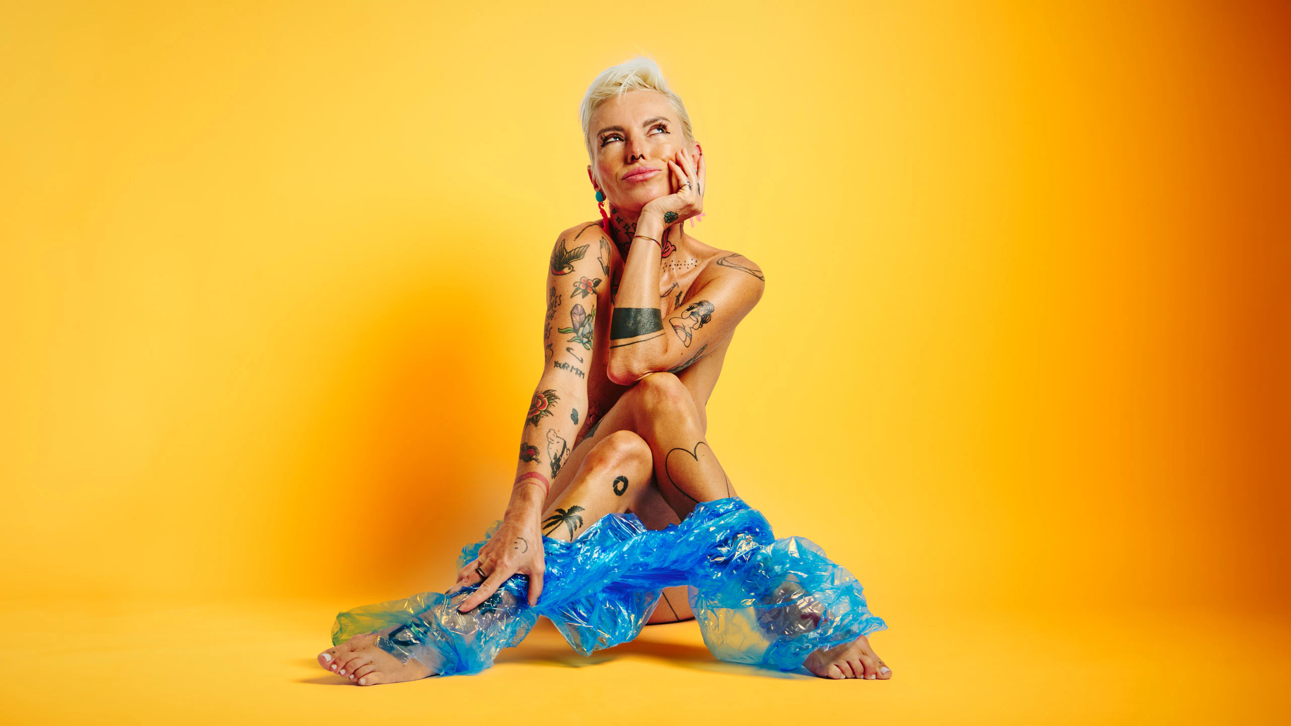 Explicit art nude portrait of Lu Epic in blue plastic pants with vivid yellow backdrop