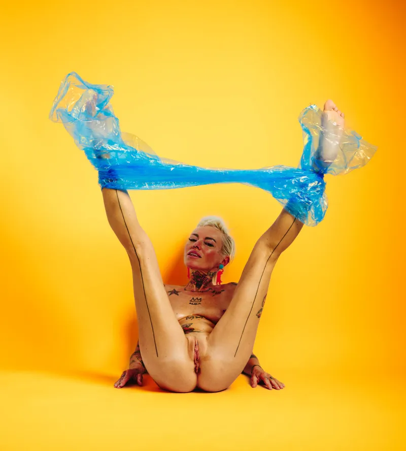 Explicit art nude portrait of Lu Epic in blue plastic pants with vivid yellow backdrop
