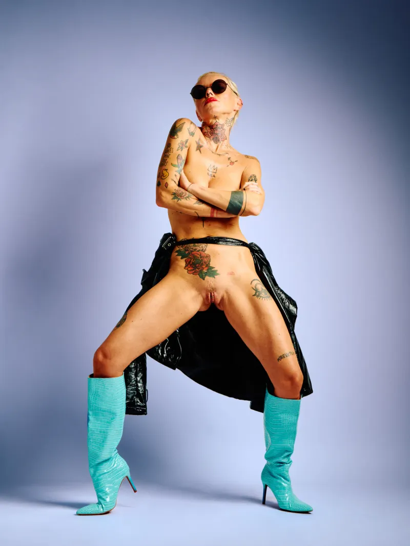 Lu Epic in an explicit nude series wearing only a black latex coat and blue boots