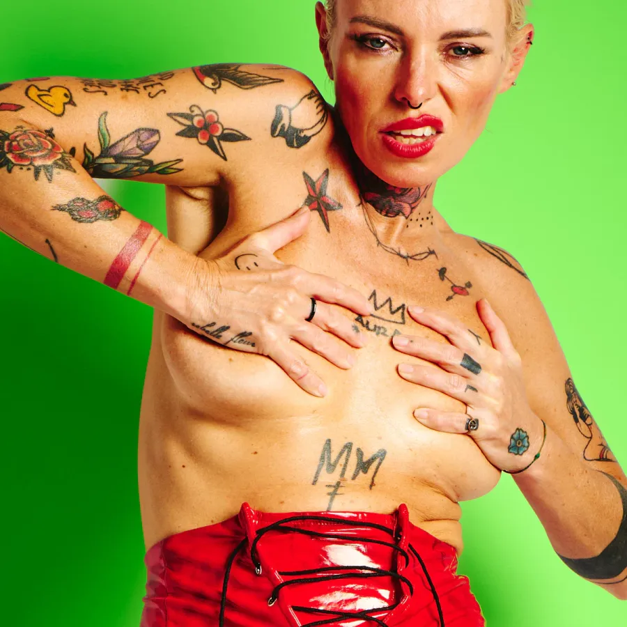Lu Epic in an energetic nude art series wearing red latex shorts and heels against green