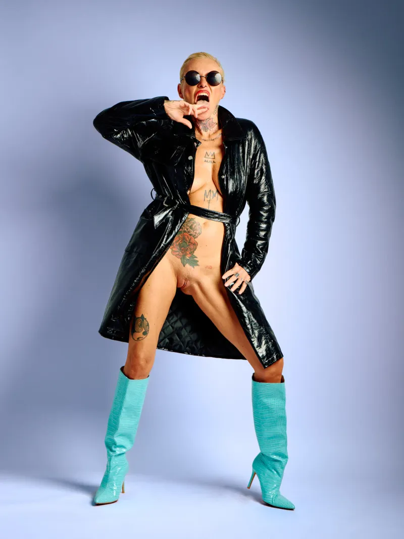 Lu Epic in an explicit nude series wearing only a black latex coat and blue boots